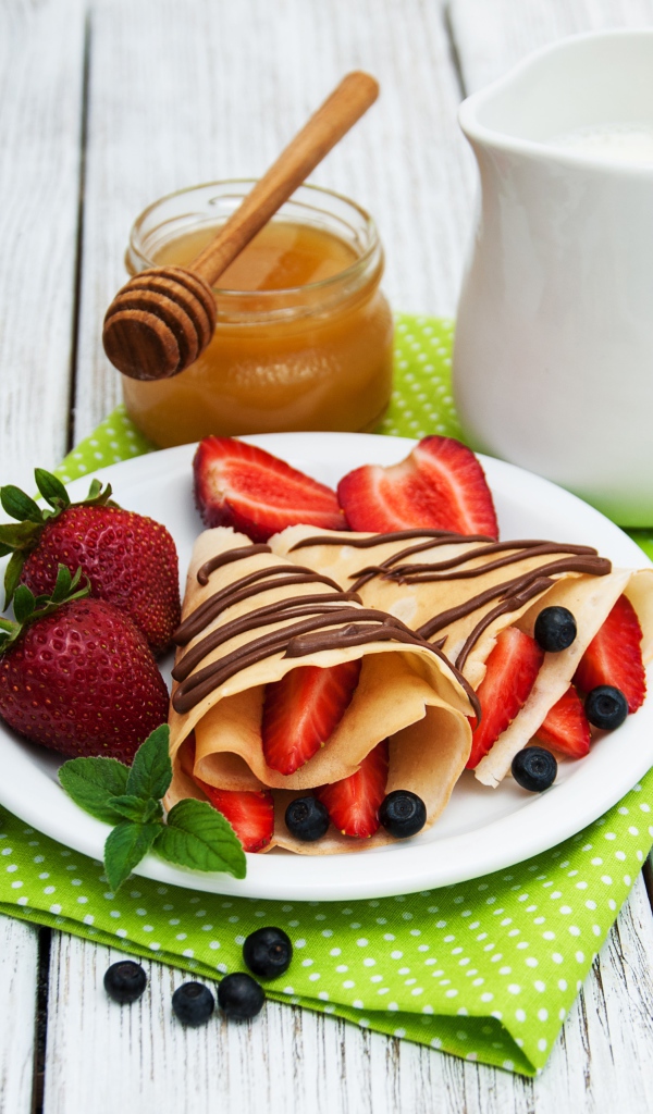 Вкусные блины с клубникой на столе с молоком и медом на праздник Масленица