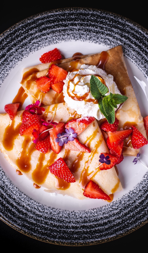 Тонкие блинчики со сливками на тарелке с клубникой и сиропом вид сверху