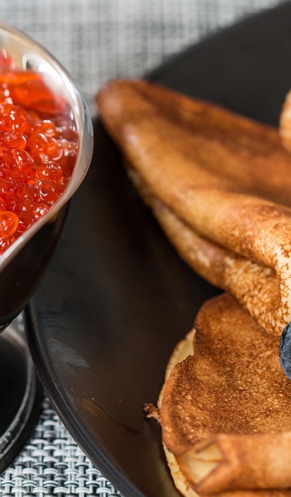 Тонкие блины с ягодами черники на столе с красной икрой на Масленицу