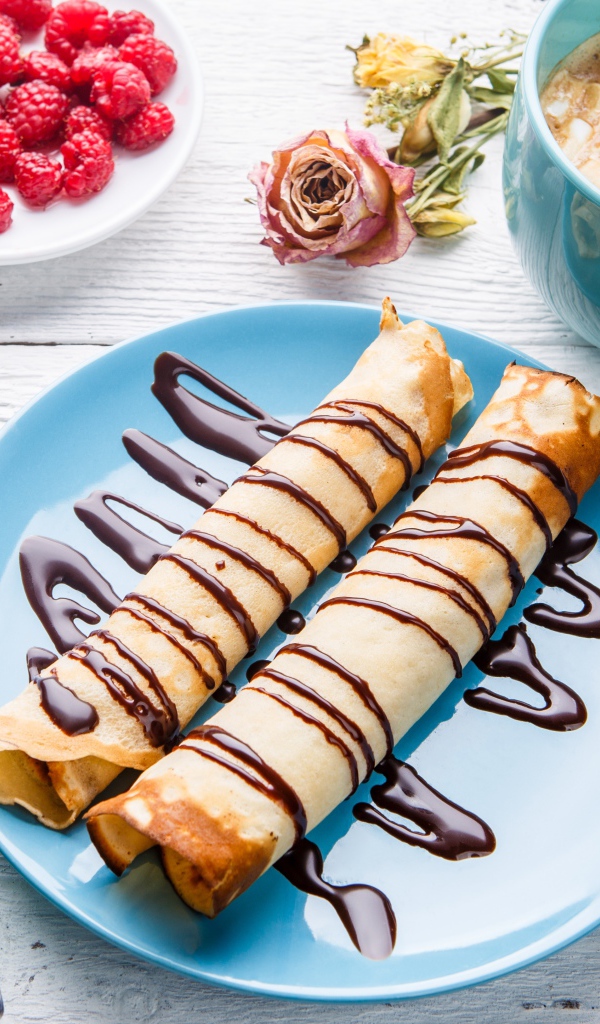 Тонкие блины с шоколадом на столе с ягодами малины и какао 