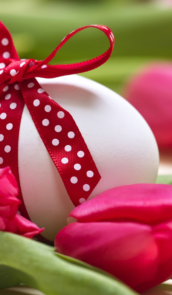 Яйцо с бантом на столе с тюльпанами на праздник Пасха