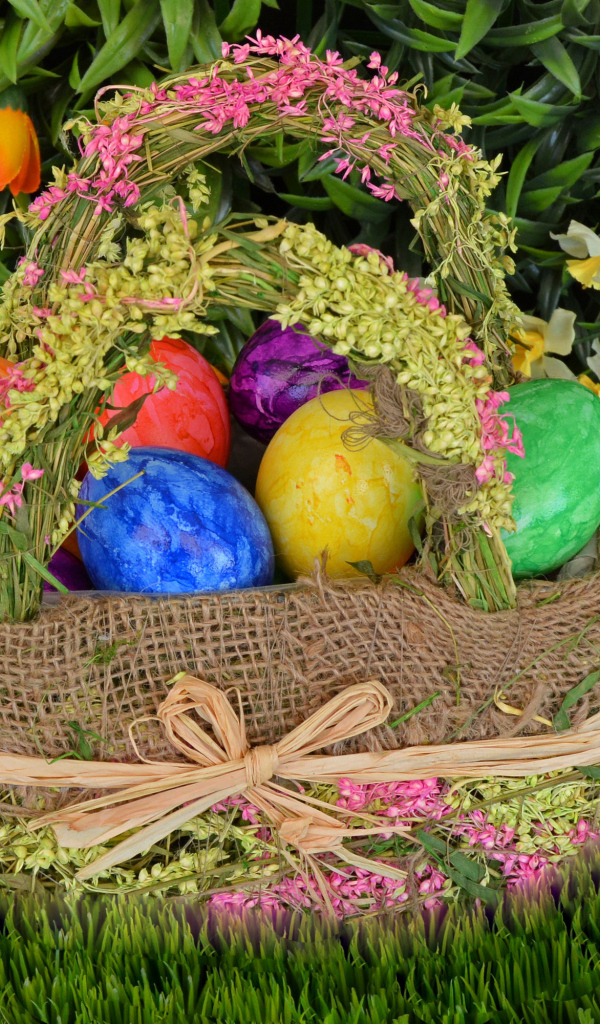 Разноцветные пасхальные яйца в корзине на зеленой траве на праздник 