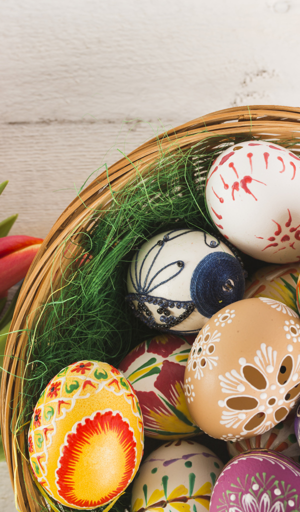 Разноцветные крашеные яйца в корзине с букетом тюльпанов на Пасху