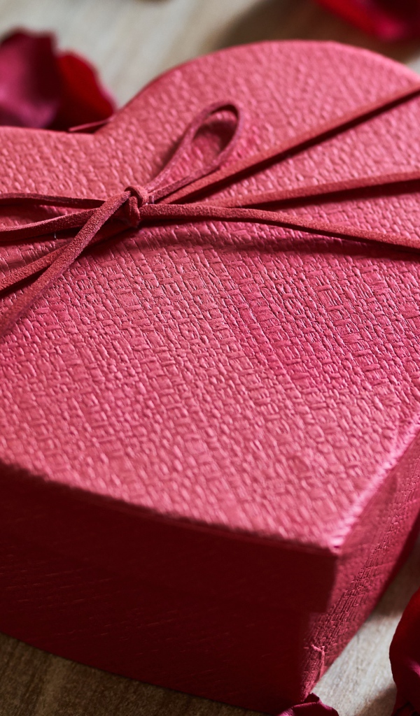 Большая красная коробка в форме сердца на столе с лепестками роз