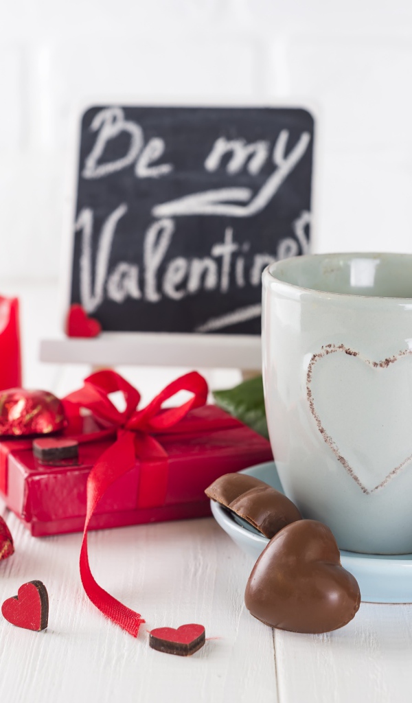Белая чашка с конфетами и красной розой на столе в подарок на 14 февраля