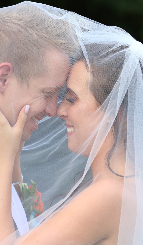 Жених и невеста стоят под белой фатой