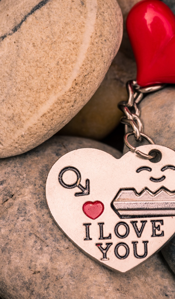 Брелок в форме сердца с ключом лежит на камнях 