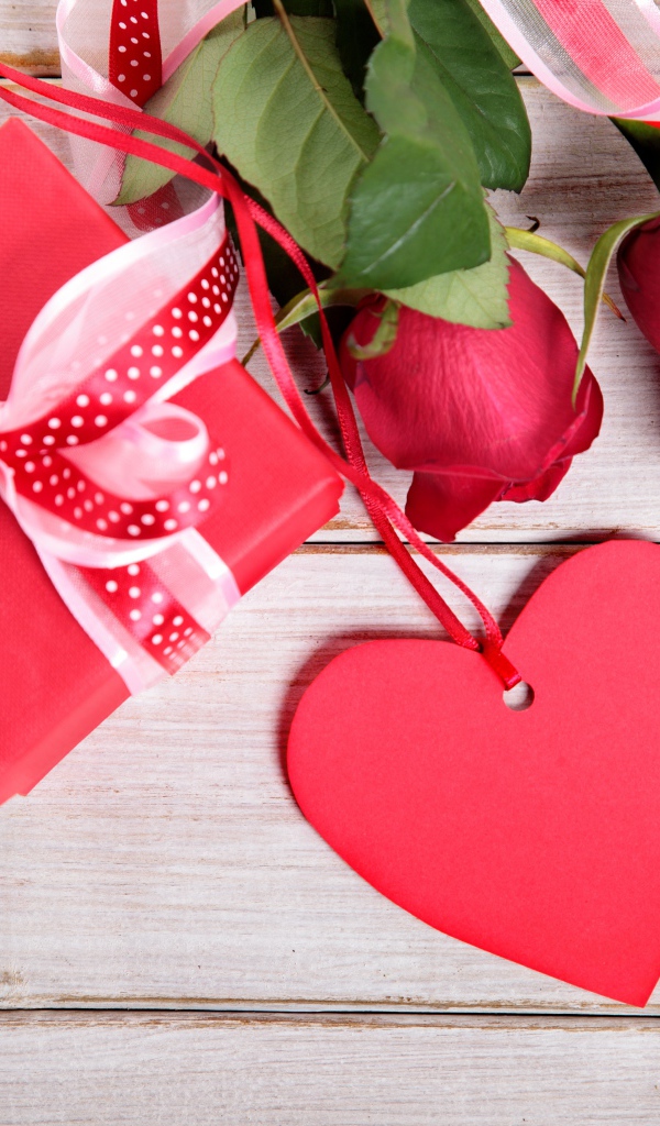 Красные розы с подарком и красным сердцем на деревянном столе