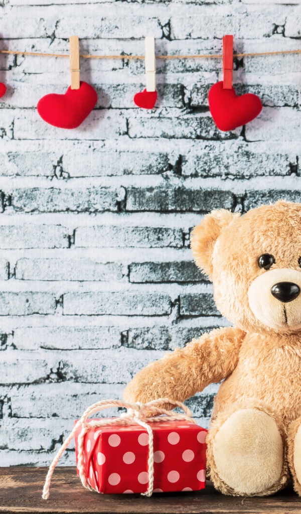 Медвежонок Тедди с подарками на фоне стены с сердечками