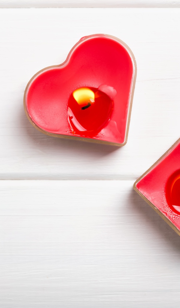 Две зажженные свечи в форме сердца на столе 