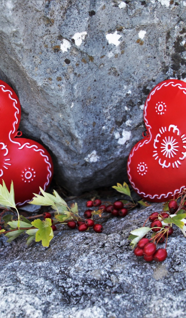 Два сердца лежат у камня с красными ягодами