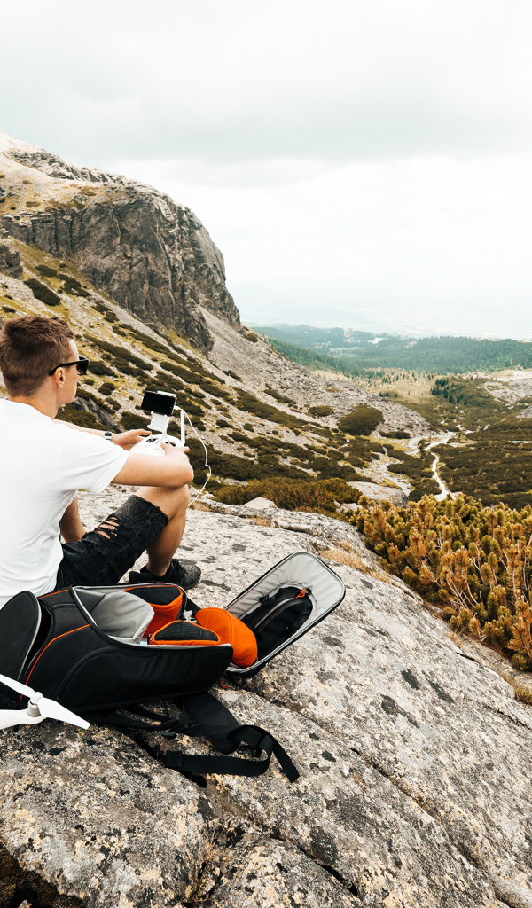 Парень с квадрокоптером сидит на камне в горах 