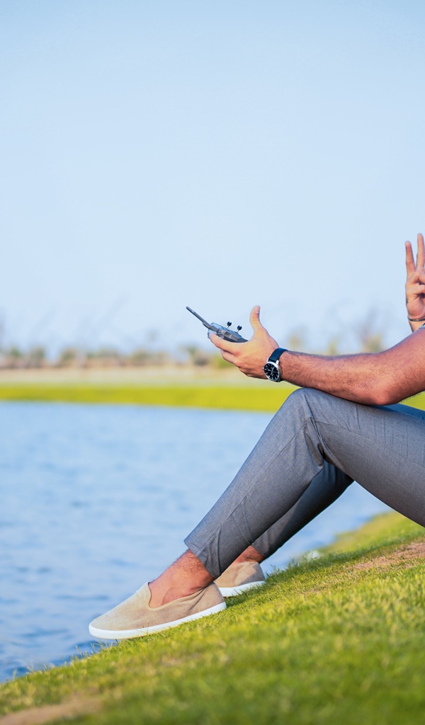 Мужчина запускает квадрокоптер над озером 