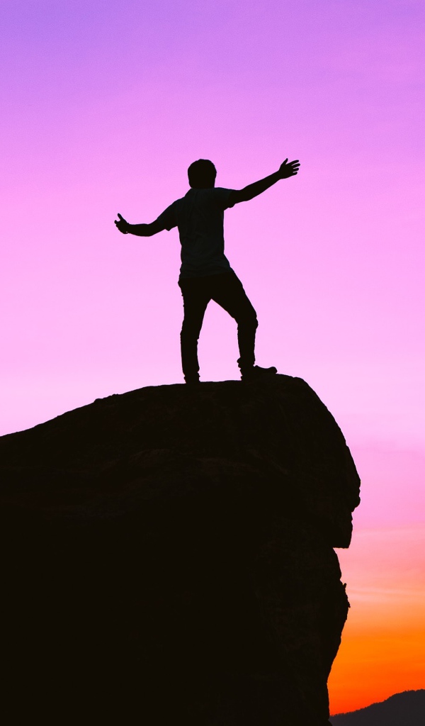 A man stands on the edge of a cliff at sunset