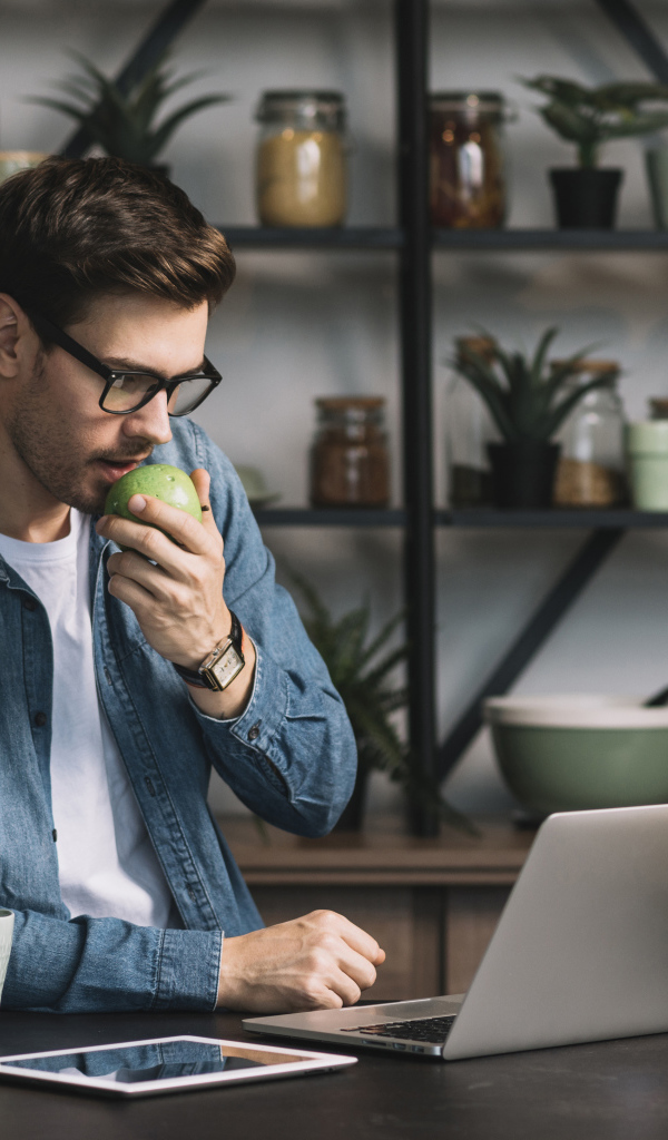Мужчина с ноутбуком ест яблоко в кафе 
