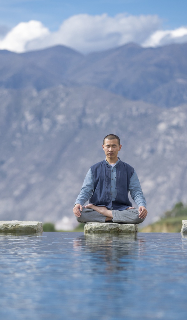 Asian man in lotus position meditates by the water.