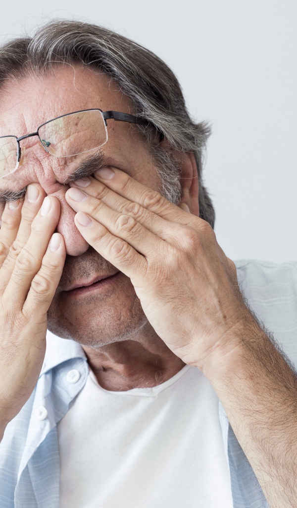 Пожилой мужчина трет глаза на сером фоне