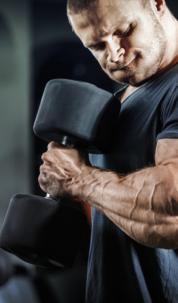 Мужчина бодибилдер в спортзале с гантелей 