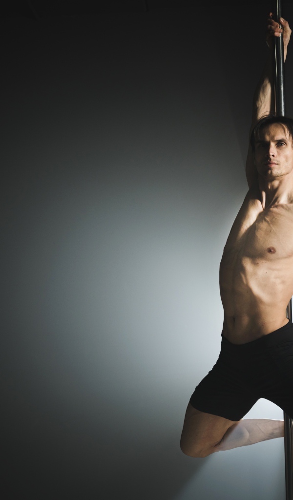 Мужчина танцует на пилоне на сером фоне