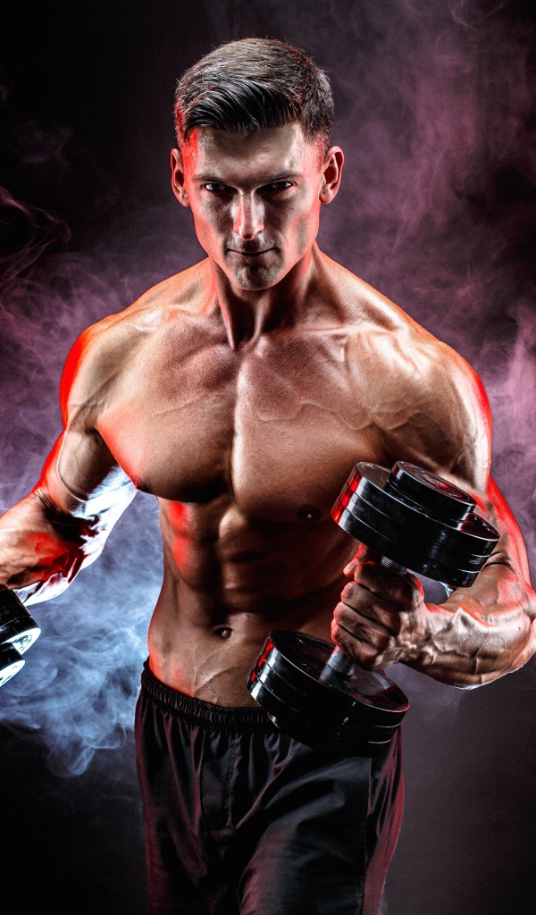 Muscular man with dumbbells in hands on a black background with smoke