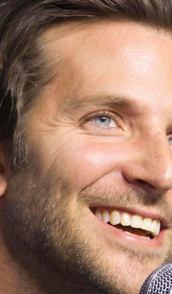 Голубоглазый актер Брэдли Купер с микрофоном на синем фоне