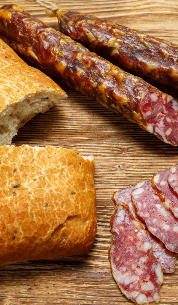 Сухая колбаса на столе с батоном и оливками