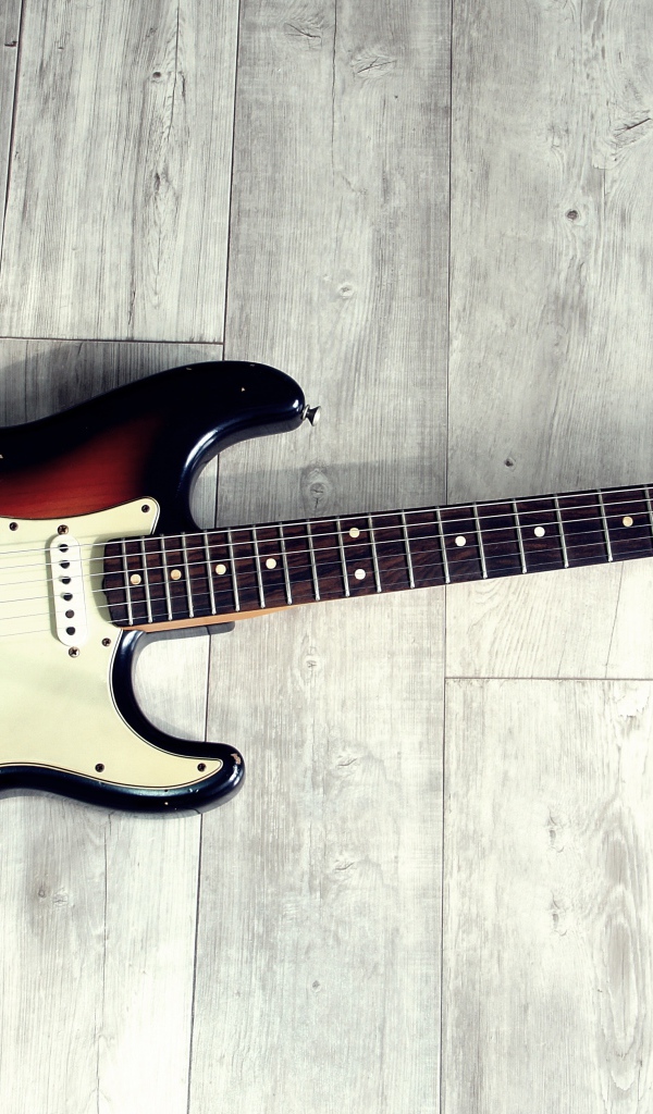 Электрогитара лежит на деревянном полу