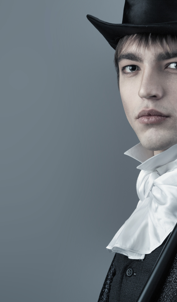 Красивый молодой человек в черном цилиндре и фраке на сером фоне