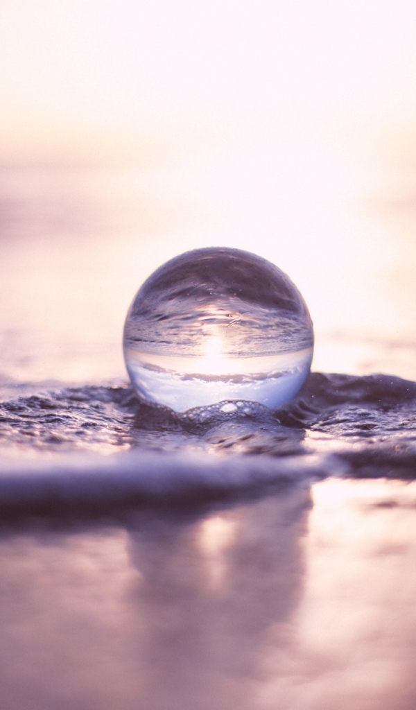 Прозрачный стеклянный шар лежит на пене в море