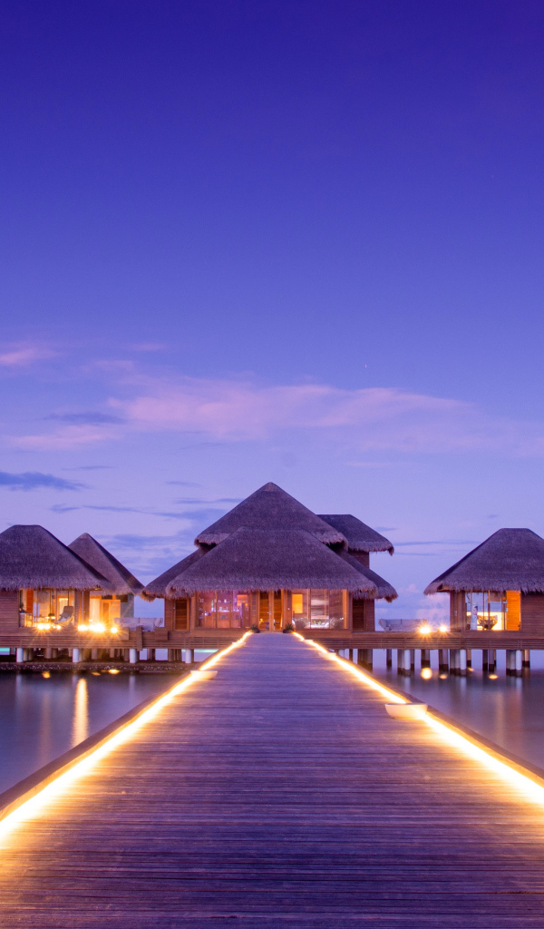 Мост с подсветкой идет к домам на сваях в океане