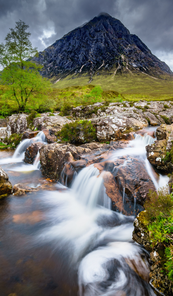 Быстрая вода в реке на фоне высокой горы под грозовым небом 