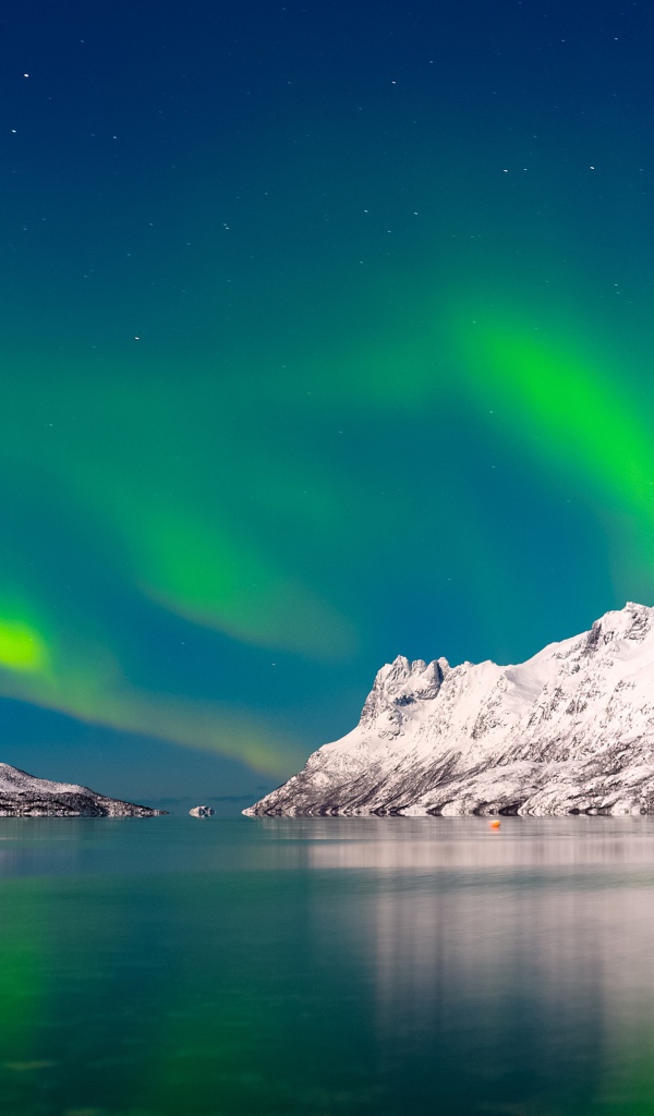 Зеленое северное сияние в небе над спокойным озером у заснеженных гор