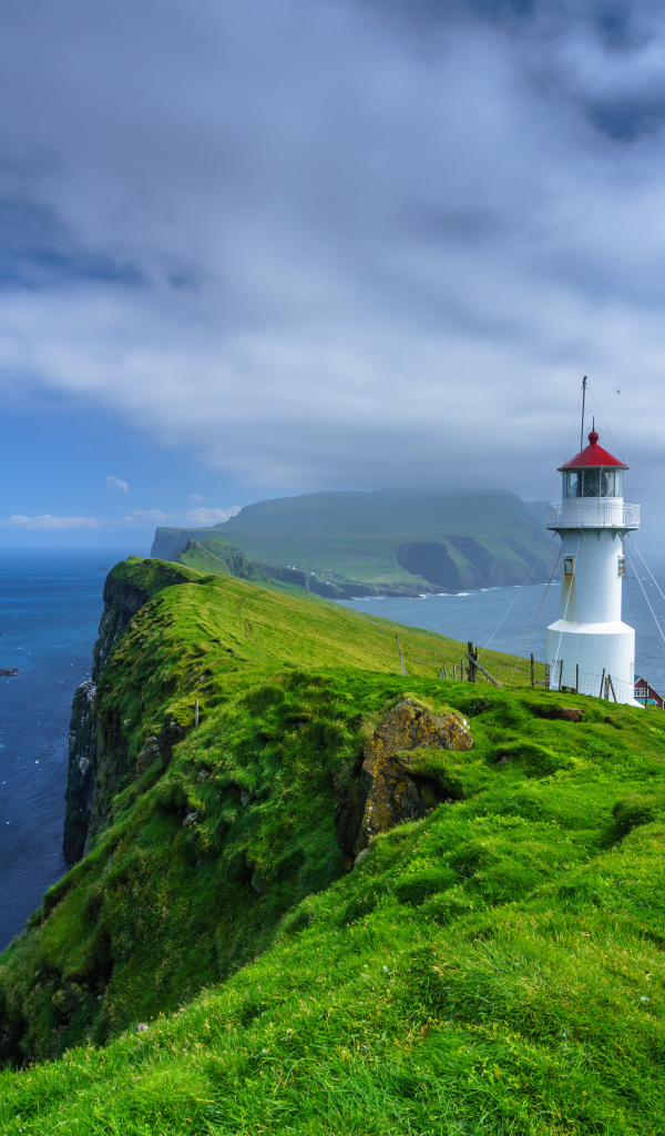 Маяк на покрытой зеленью скале под голубым небом