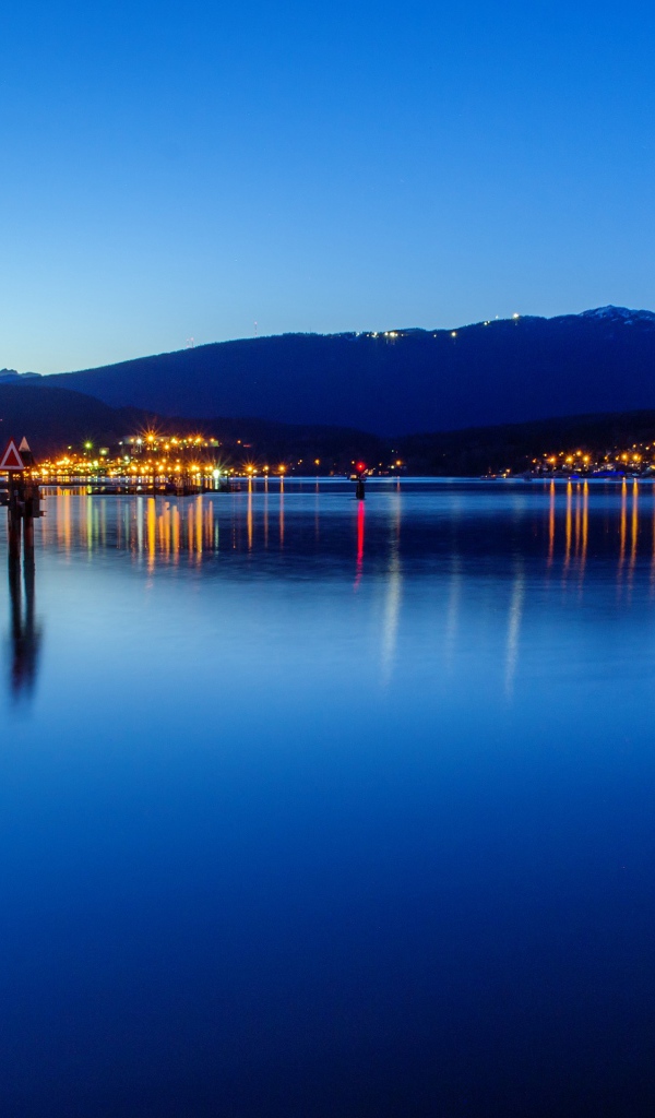 Огни ночного города отражаются в воде у гор 
