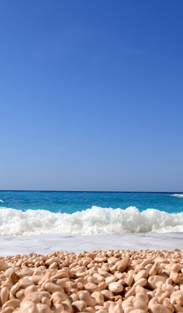 Красивая голубая вода с белыми волнами на пляже с галькой 