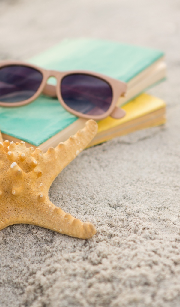 Книги, очки и морская звезда на белом песке 