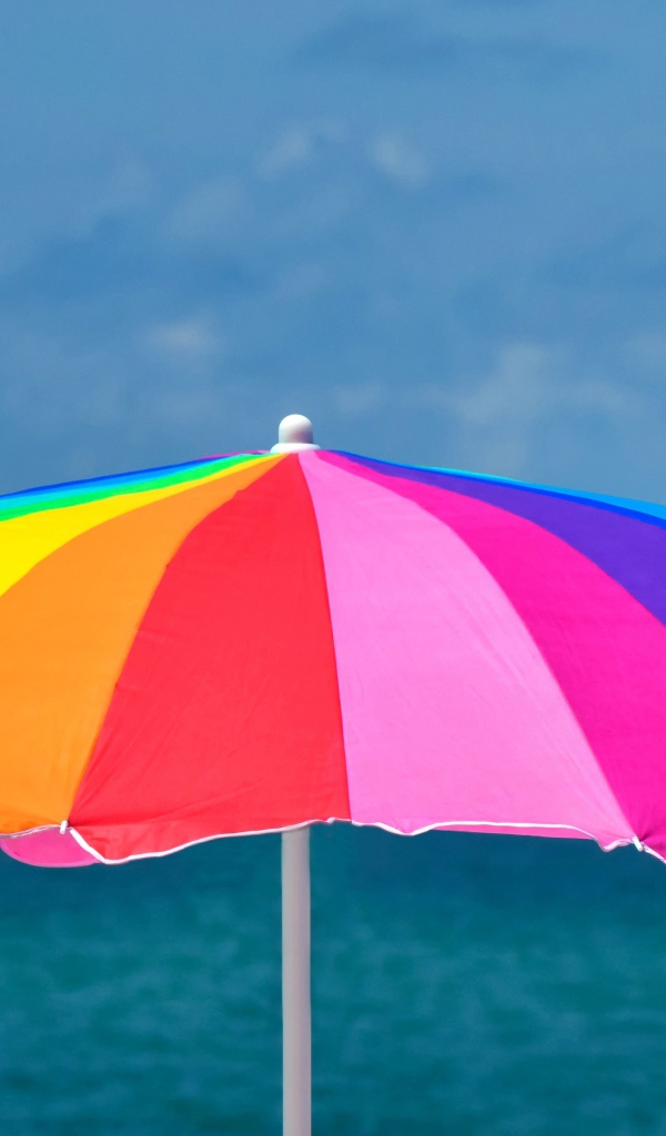 Большой разноцветный пляжный зонт на фоне моря