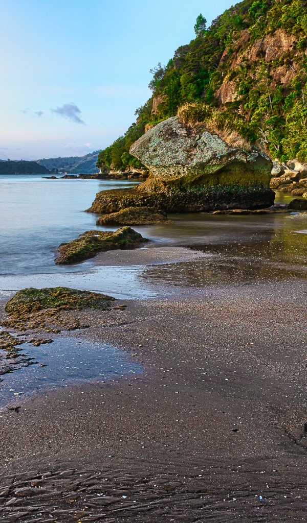 Мокрый песок и большие каменные глыбы на берегу залива