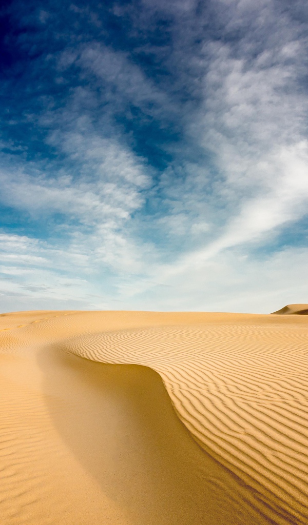 Песчаная дюна под голубым небом с белыми облаками 