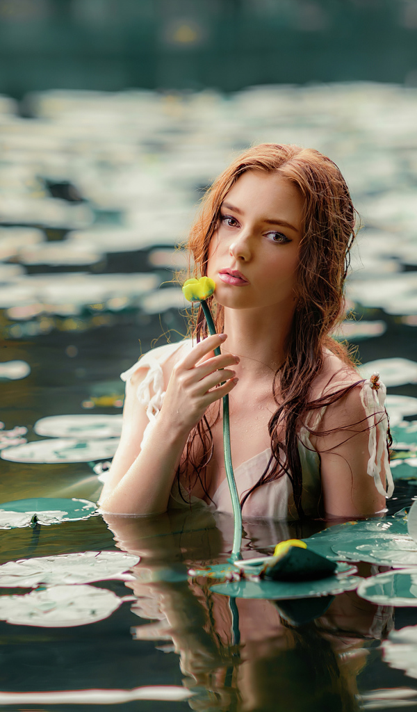 Красивая молодая девушка с водяными лилиями в пруду