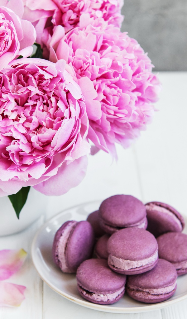 Букет розовых пионов на белом столе с десертом макарон 