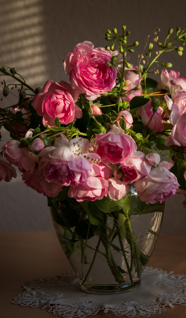 Букет розовых роз в стеклянной вазе не столе в лучах солнца 