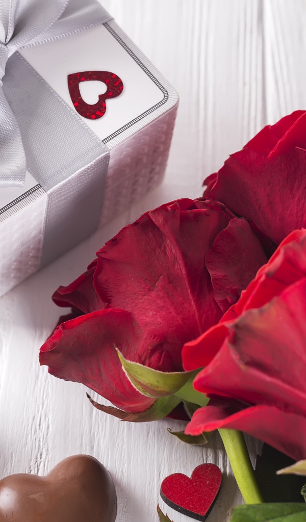 Букет красных роз на столе с конфетами и подарком