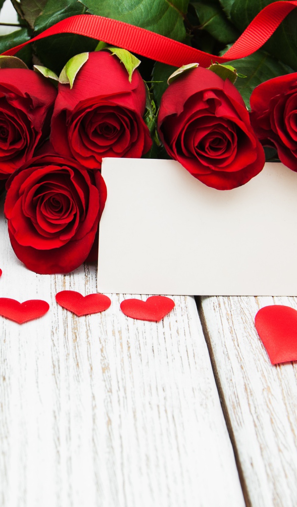 Букет красных роз на столе с сердечками и открыткой