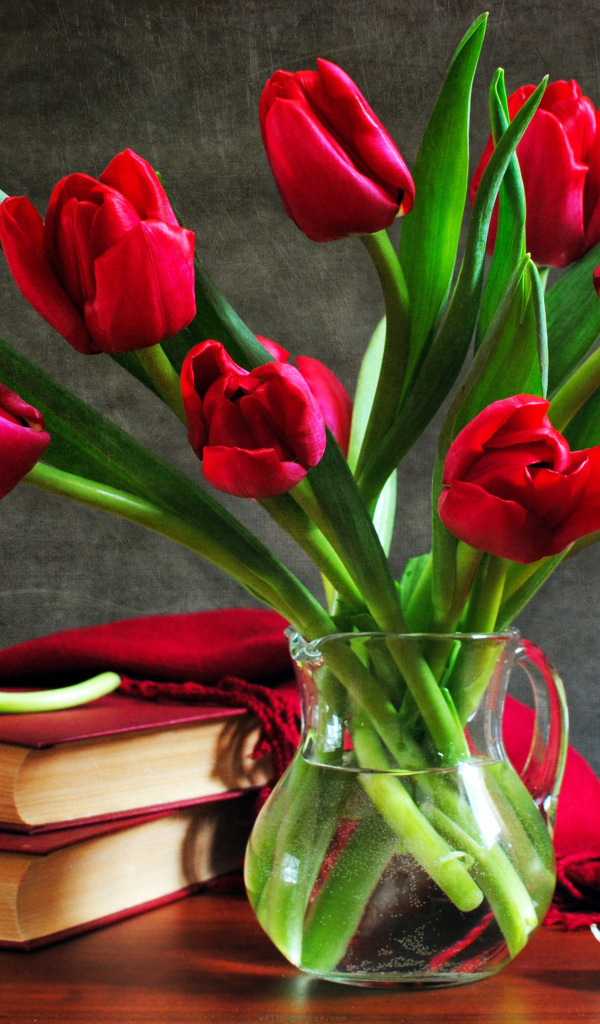 Букет красных тюльпанов в вазе на столе с шарфом и книгами