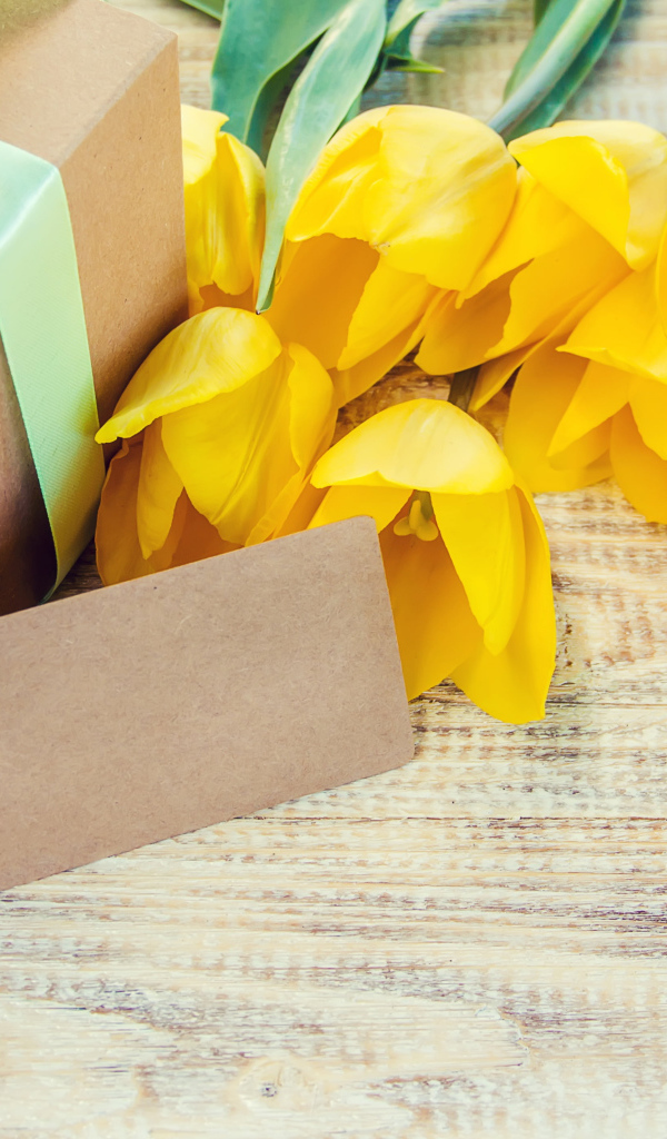 Букет желтых тюльпанов с подарком на столе 