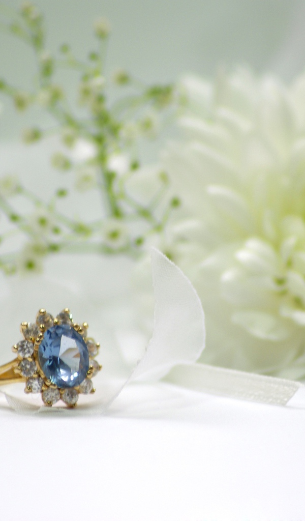 Дорогое кольцо с камнем на столе с белым цветком