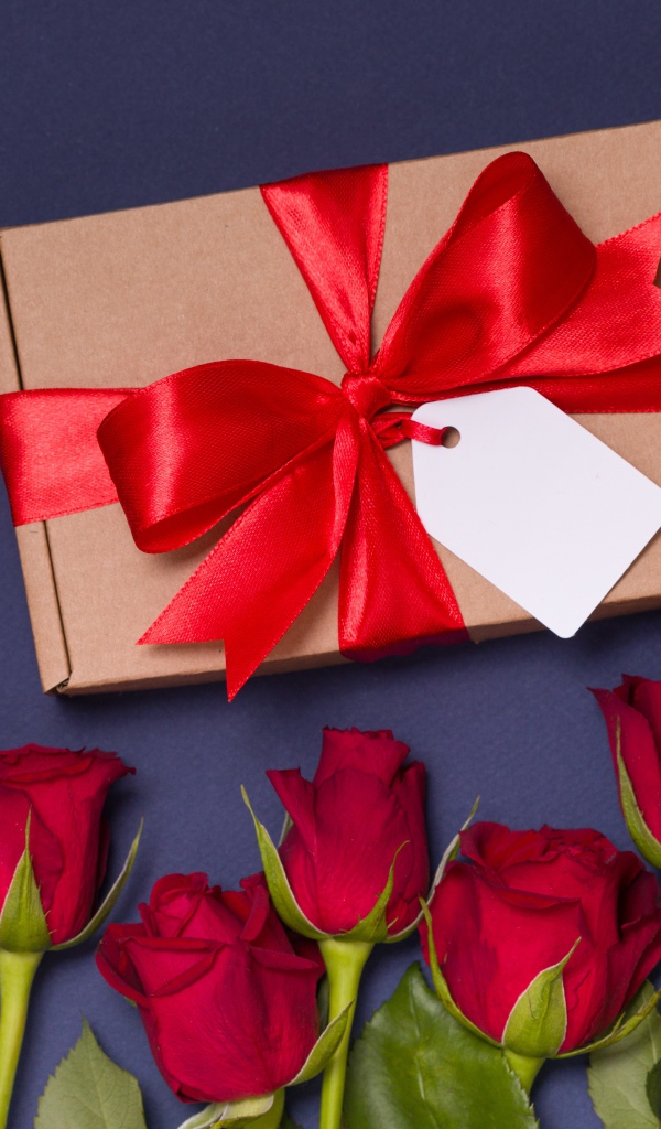 Подарок с красным бантом на столе с розами