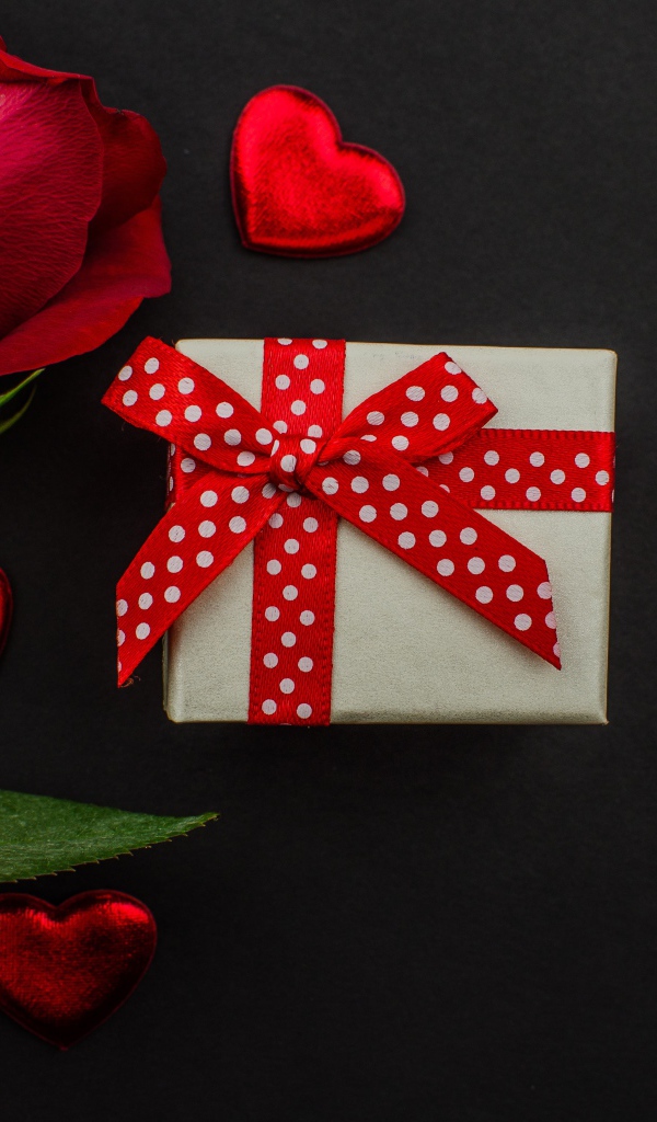 Маленький подарок и красная роза на черном столе