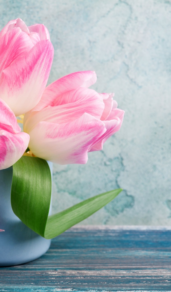 Три розовых тюльпана в чашке на столе 